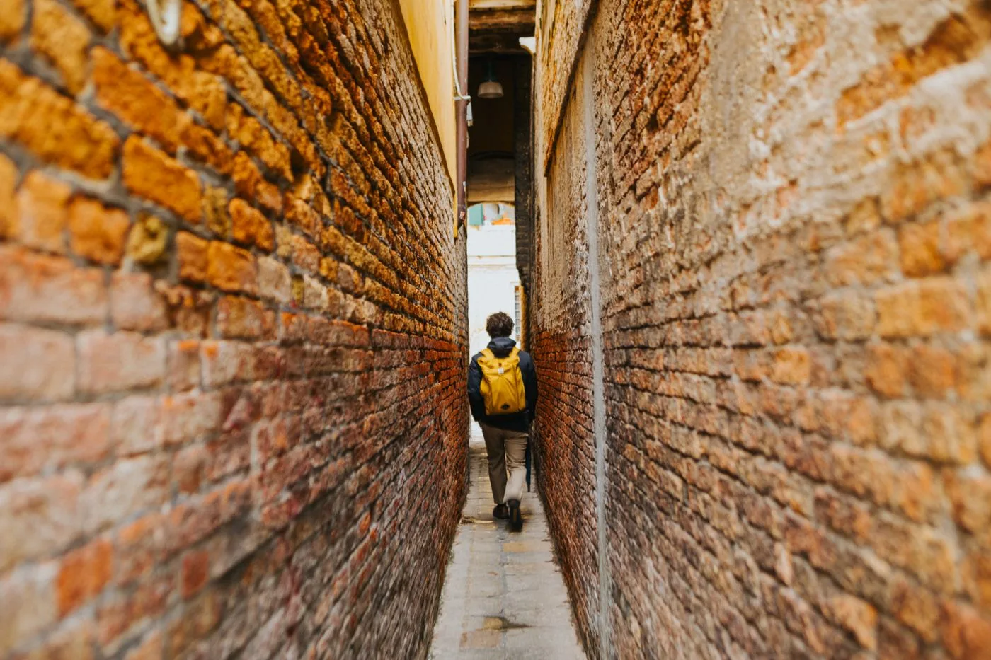 黄色いリュックを背負ってれんがの細い路地を歩く旅行者の後ろ姿