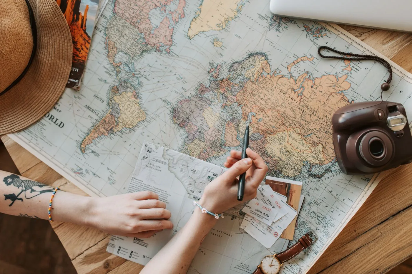 世界地図の上で、ペンを持って旅行の準備をしている人の手元