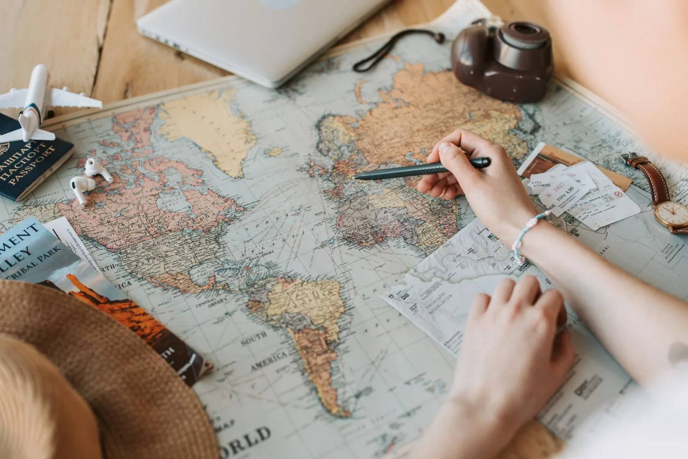 世界地図の上でペンを持ち、旅先に印を付けて予定を立てる手元