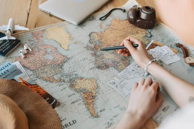 世界地図の上でペンを持ち、旅先に印を付けて予定を立てる手元