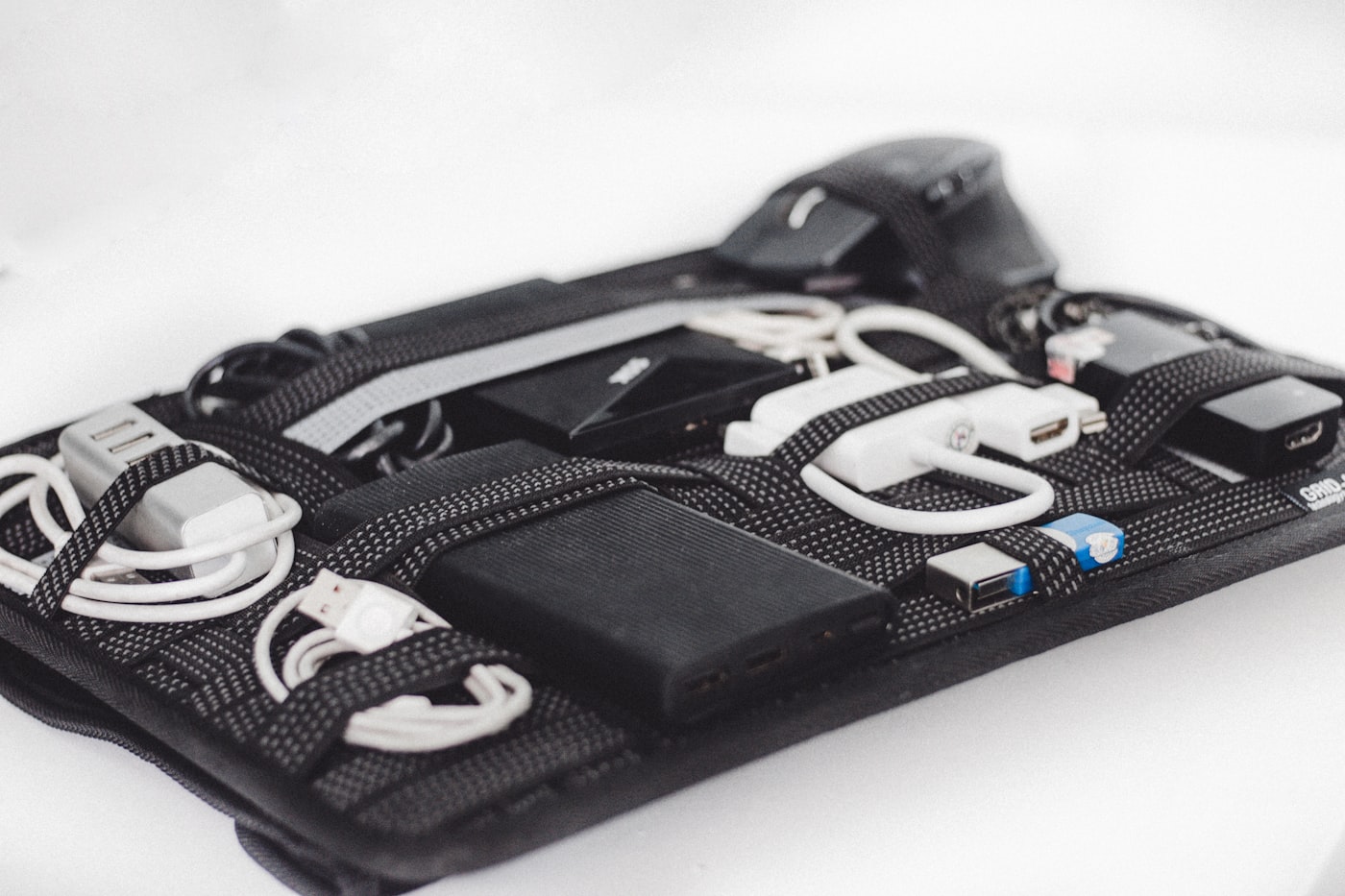 白い背景に置かれたガジェット整理ポーチ。中央に複数のUSBポートを備えた黒いモバイルバッテリーが固定され、周囲に充電ケーブルやUSBハブが並んでいる