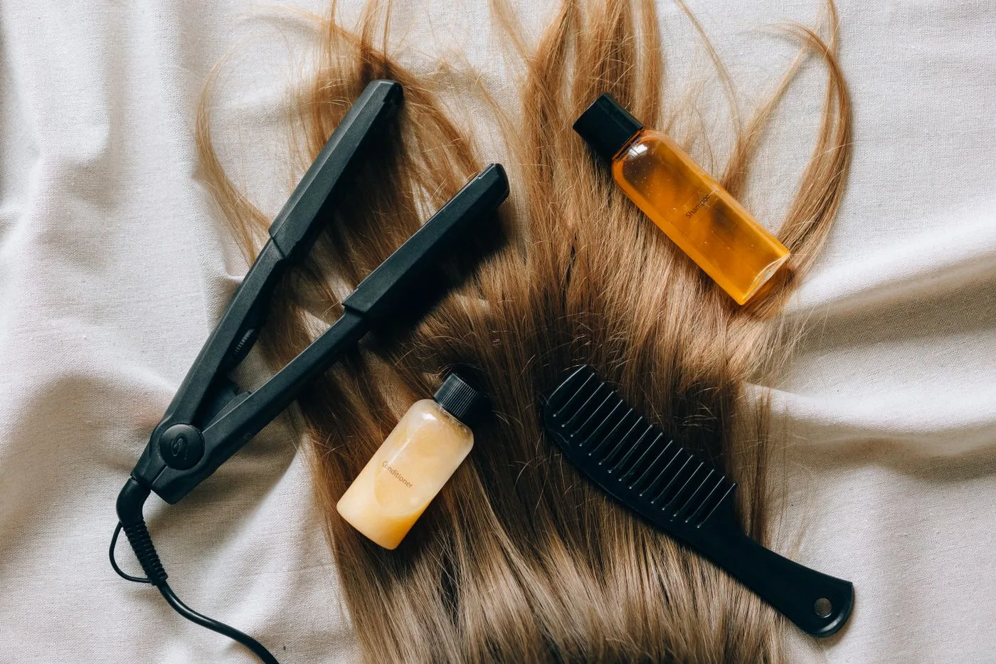 白い布の上に置いたヘアアイロンとくし、旅行用の小分けボトル