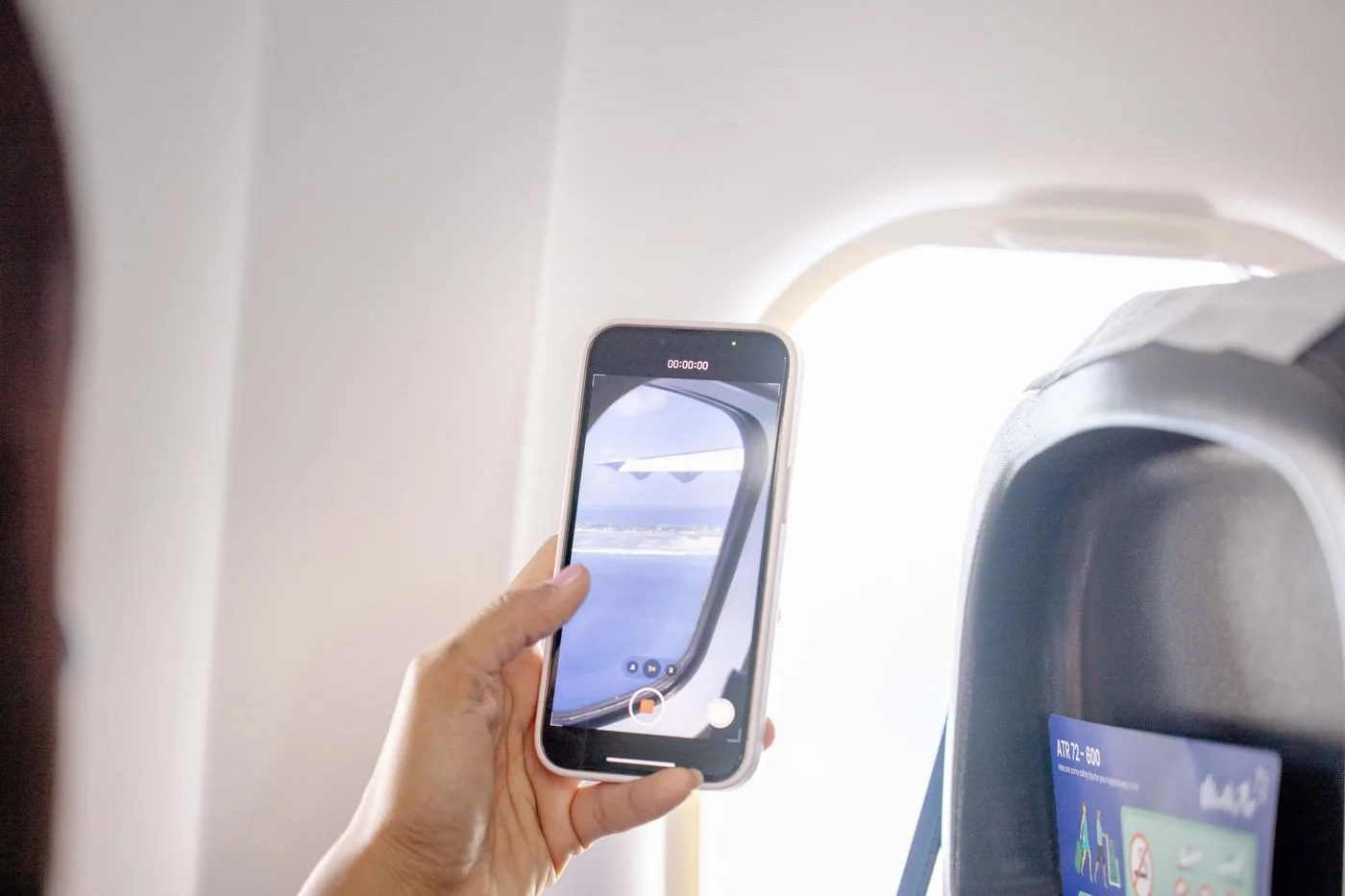飛行機の窓際でスマートフォンを手に持つ旅行者の手元