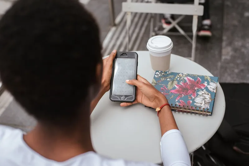 屋外のカフェのテーブルで、スマートフォンのカレンダーを開いている人の手元
