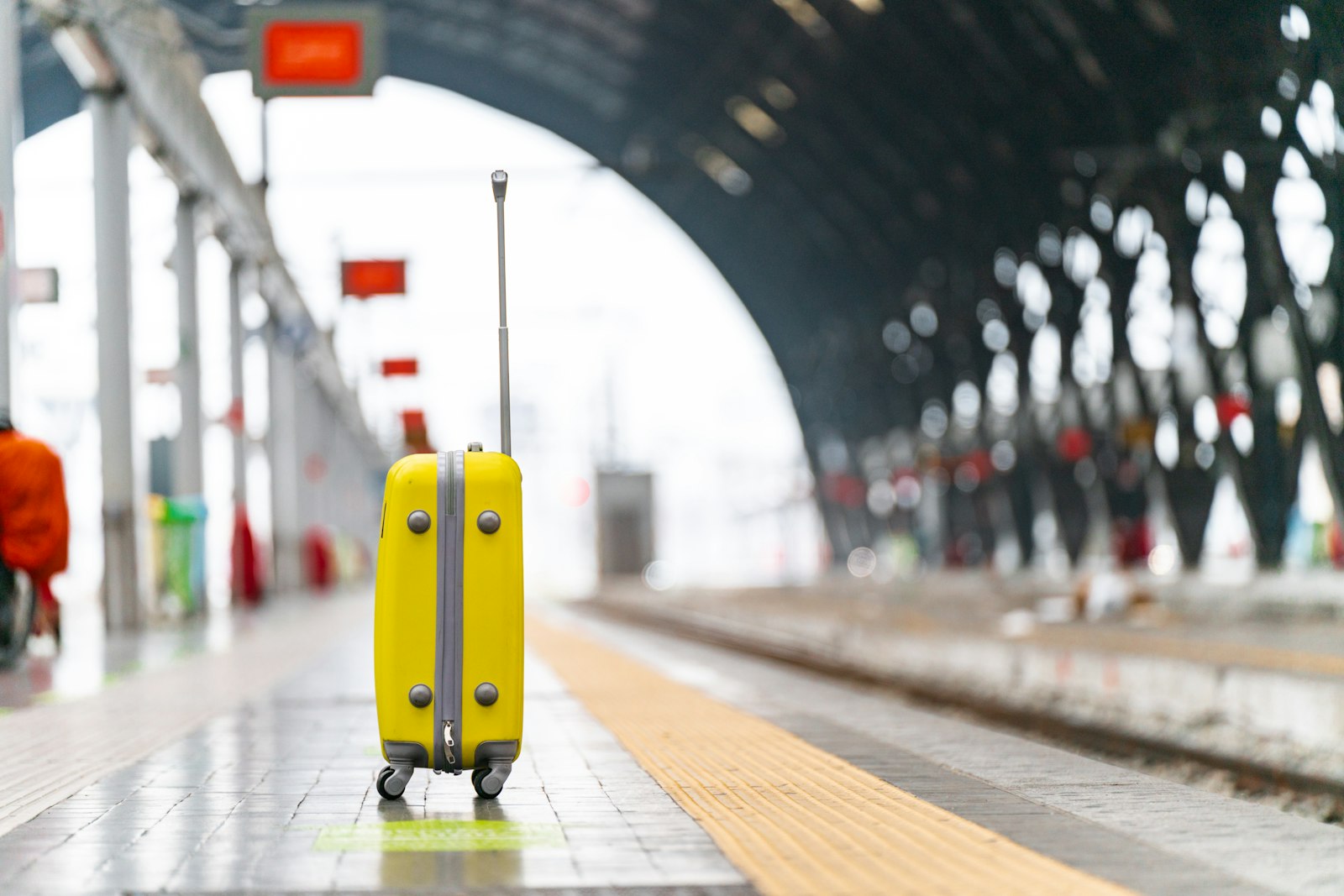 駅のホームに置かれた黄色い機内持ち込みサイズのスーツケース