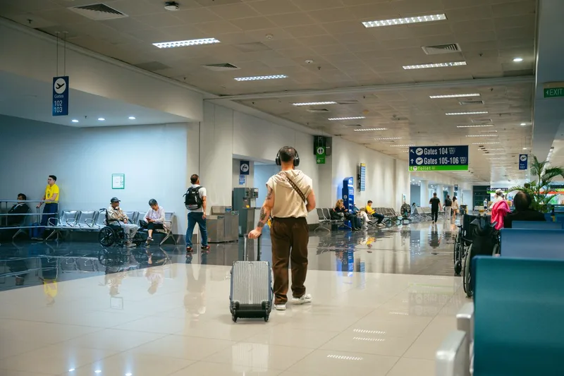空港の通路でスーツケースを引いて歩く人と、その奥をリュックを背負って歩く人