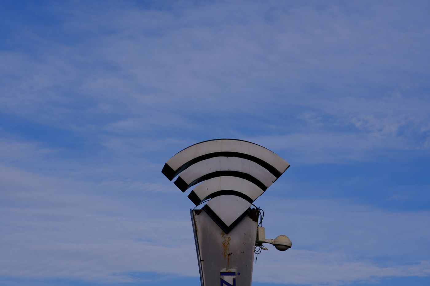 青空を背景に立つ、Wi-Fiの電波マークをかたどった白い屋外サイン